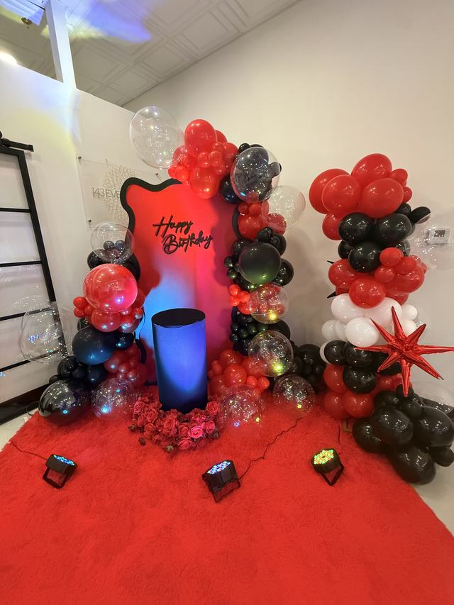 Red Happy Birthday backdrop with red and black balloon garland, pedestal, and red carpet