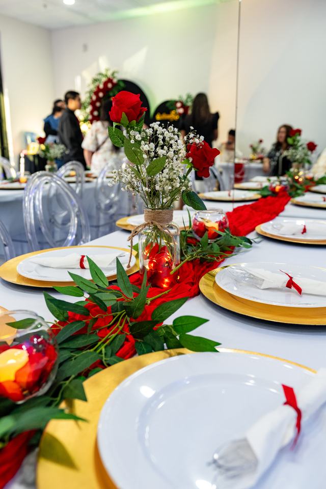 Close-up of a red rose centerpiece on a table set with gold chargers and white plates