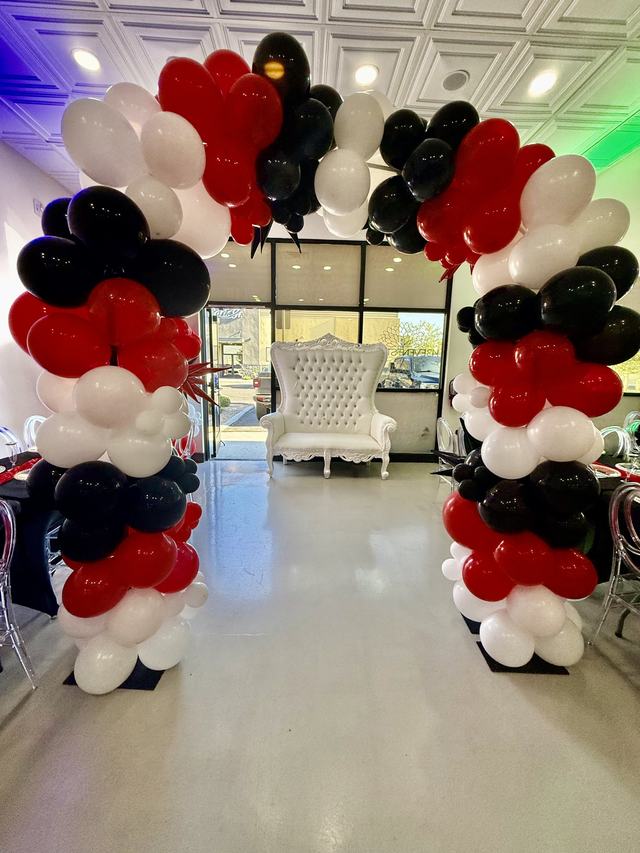 White tufted throne chair framed by a red, black, and white balloon arch