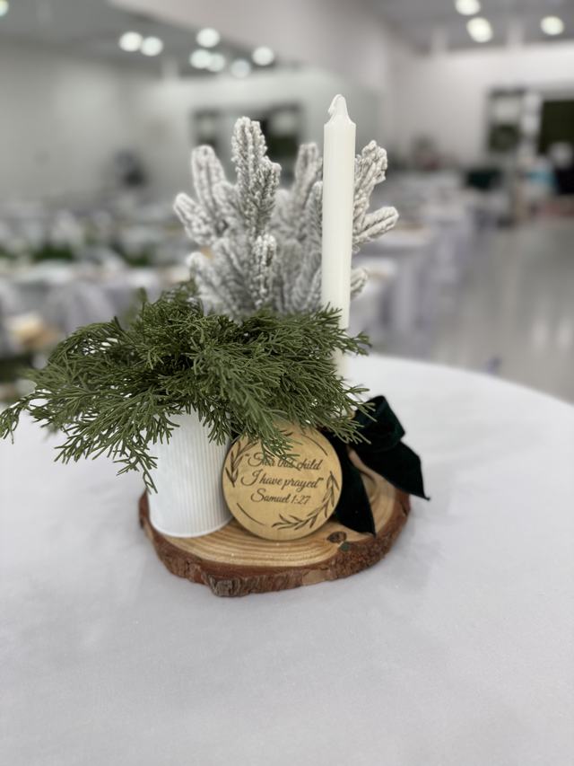 Winter centerpiece with flocked greenery and a candle on a wood slice